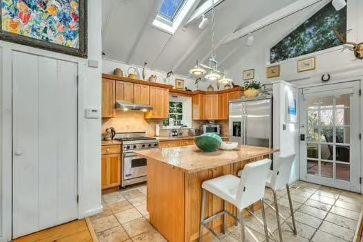 kitchen with lofted ceiling with skylight, a center island, a kitchen breakfast bar, stainless steel appliances, and backsplash