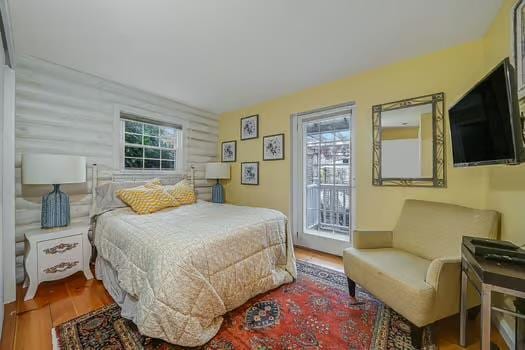 bedroom with wood-type flooring, log walls, and access to outside