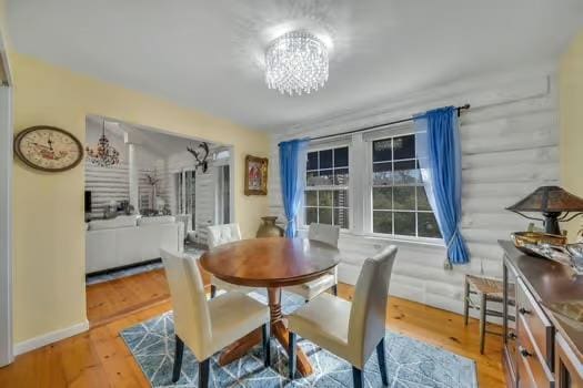 dining space featuring an inviting chandelier, light hardwood / wood-style floors, and rustic walls