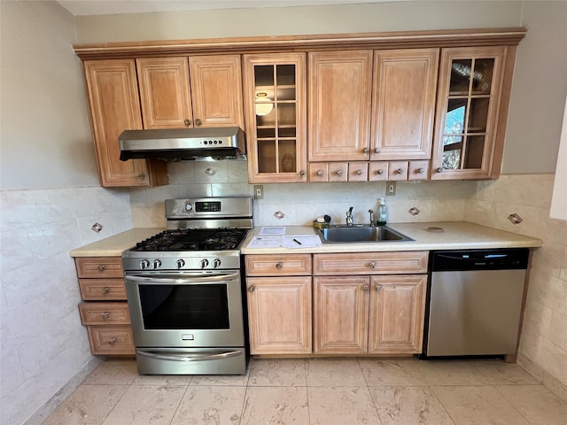 kitchen featuring stainless steel appliances, sink, and tile walls