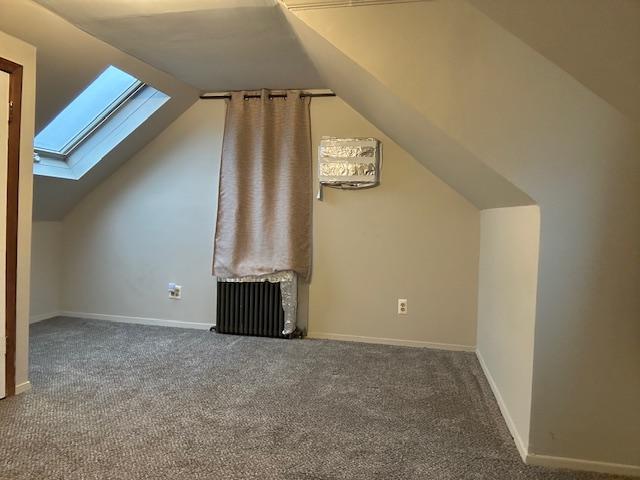 bonus room featuring radiator, vaulted ceiling with skylight, and carpet flooring