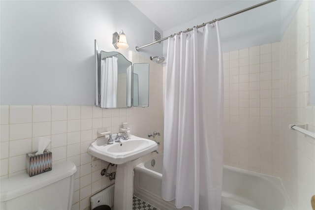 bathroom with toilet, shower / bath combo with shower curtain, and tile walls