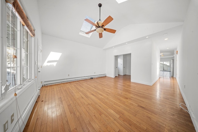 empty room featuring vaulted ceiling with skylight, light wood-style flooring, a baseboard heating unit, a ceiling fan, and baseboards