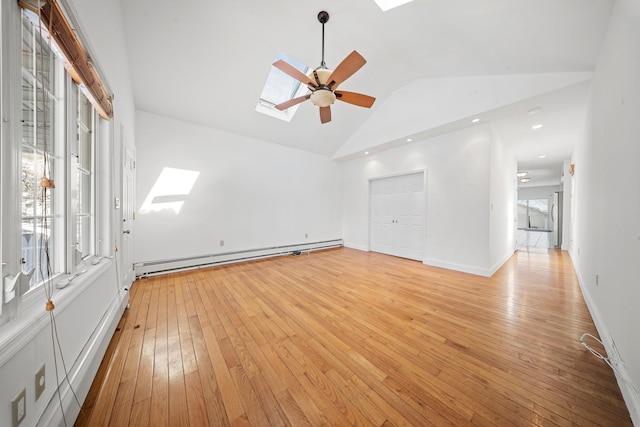 empty room featuring light wood finished floors, a baseboard radiator, lofted ceiling with skylight, ceiling fan, and baseboards