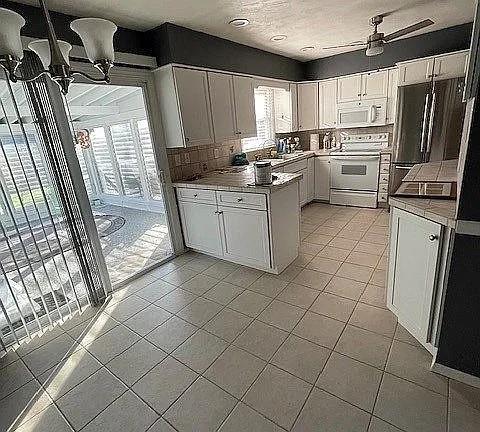 kitchen with white appliances, ceiling fan, white cabinetry, light tile patterned flooring, and decorative backsplash