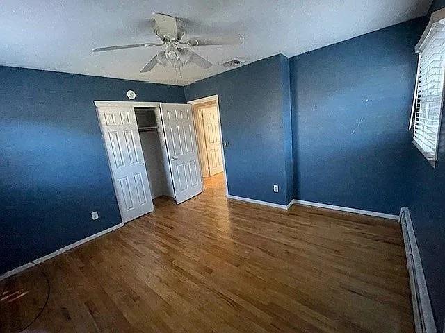 unfurnished bedroom featuring a textured ceiling, baseboard heating, dark hardwood / wood-style flooring, a closet, and ceiling fan