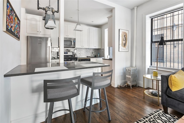 kitchen featuring appliances with stainless steel finishes, radiator, pendant lighting, white cabinetry, and kitchen peninsula