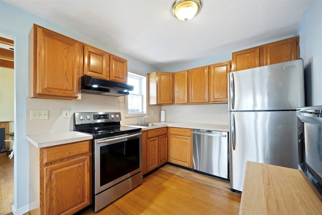 kitchen with appliances with stainless steel finishes, sink, and light hardwood / wood-style floors