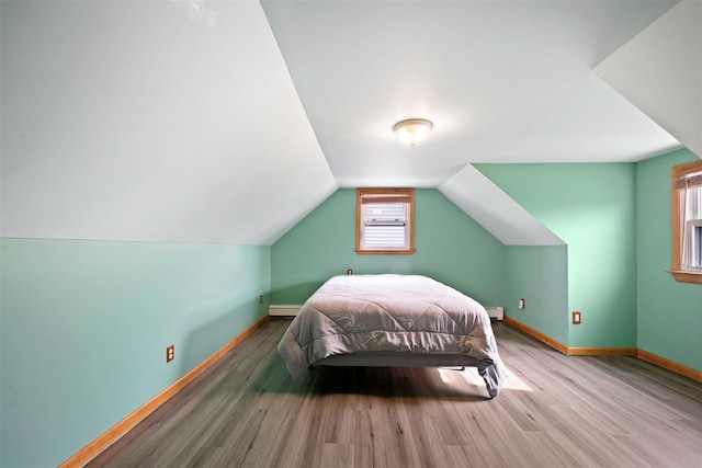 unfurnished bedroom featuring a baseboard radiator, lofted ceiling, hardwood / wood-style floors, and multiple windows