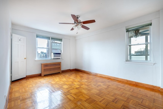 spare room with a healthy amount of sunlight, ceiling fan, radiator, and light parquet flooring