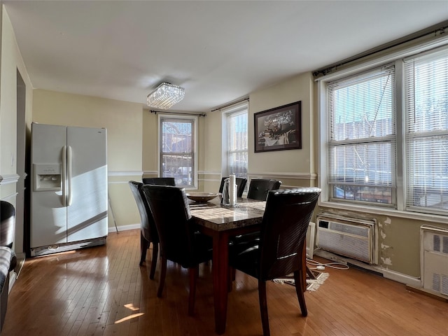 dining space with radiator heating unit, an AC wall unit, and light wood-type flooring