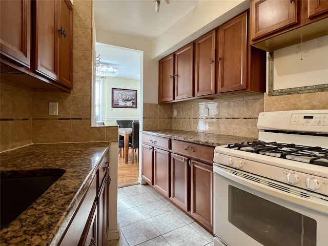 kitchen with white gas stove, decorative backsplash, light tile patterned floors, and dark stone counters