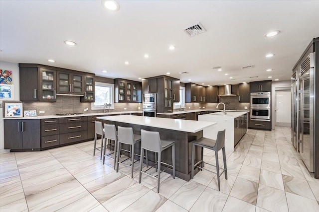 kitchen with wall chimney range hood, sink, a breakfast bar, appliances with stainless steel finishes, and a spacious island