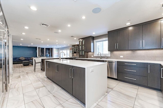 kitchen with tasteful backsplash, stainless steel dishwasher, a large island, and sink