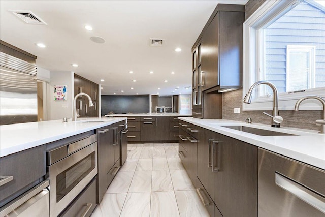 kitchen with stainless steel microwave, sink, dark brown cabinets, and backsplash