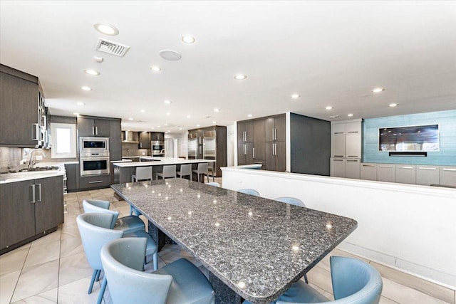 kitchen featuring sink, a breakfast bar area, light tile patterned floors, dark brown cabinetry, and a spacious island