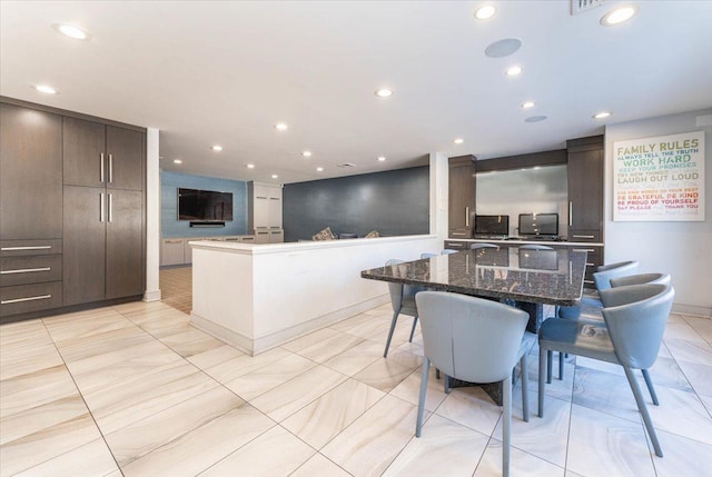 kitchen with a kitchen bar, a large island, dark brown cabinetry, and dark stone counters