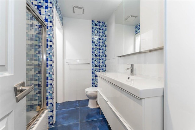 full bathroom featuring combined bath / shower with glass door, tile walls, vanity, toilet, and tile patterned floors