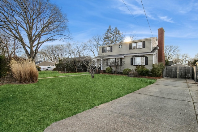 view of front of house with concrete driveway, a chimney, a front yard, and a gate