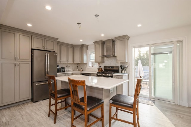 kitchen featuring light countertops, wall chimney range hood, appliances with stainless steel finishes, gray cabinets, and a kitchen bar