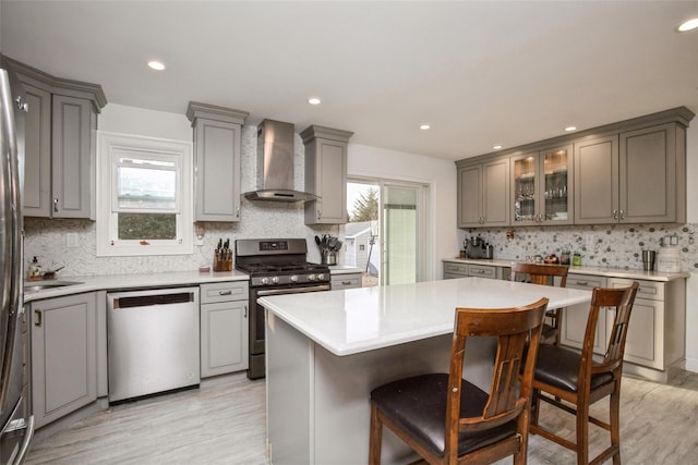 kitchen featuring appliances with stainless steel finishes, gray cabinets, light countertops, and wall chimney range hood