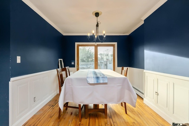 dining area with a baseboard radiator, light wood-style flooring, ornamental molding, wainscoting, and an inviting chandelier