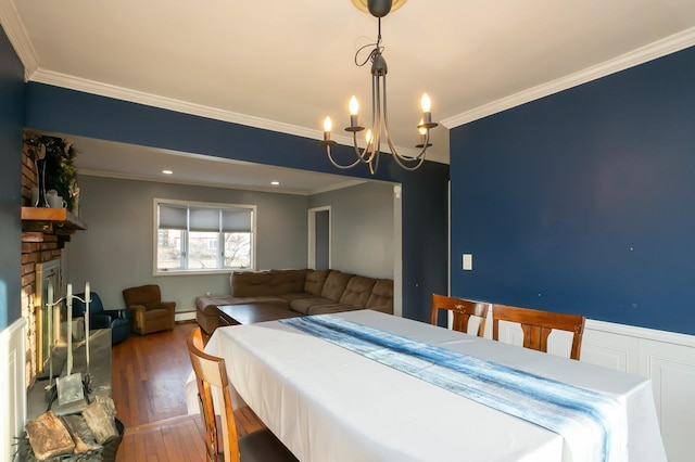 dining space with crown molding, a fireplace, wood finished floors, and an inviting chandelier