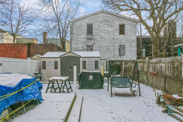 snow covered back of property featuring a storage unit