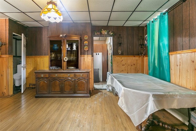 dining room with wooden walls, light hardwood / wood-style flooring, and a drop ceiling