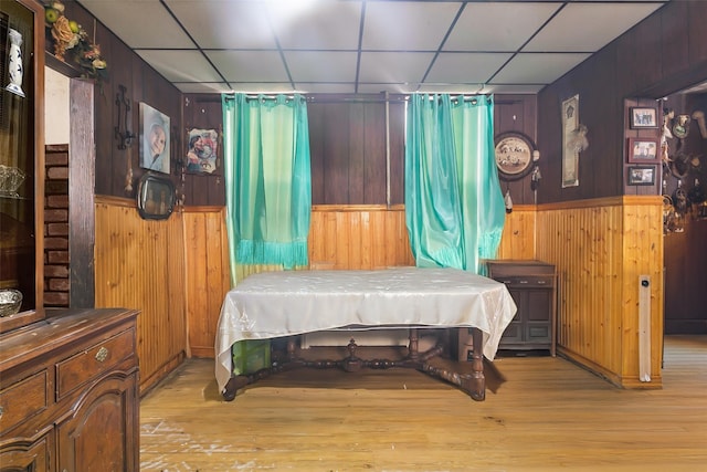 bedroom featuring light hardwood / wood-style flooring, wooden walls, and a paneled ceiling