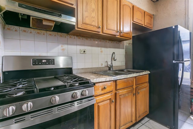 kitchen featuring light tile patterned flooring, sink, gas range, black refrigerator, and backsplash