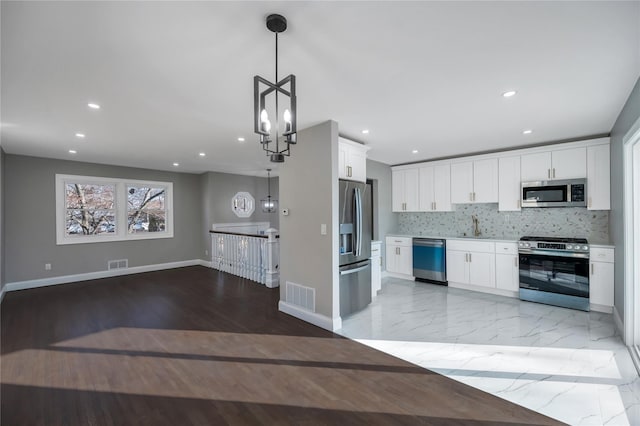 kitchen with tasteful backsplash, appliances with stainless steel finishes, decorative light fixtures, and white cabinets