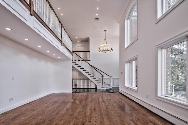 unfurnished living room featuring dark hardwood / wood-style flooring, a baseboard heating unit, and a towering ceiling