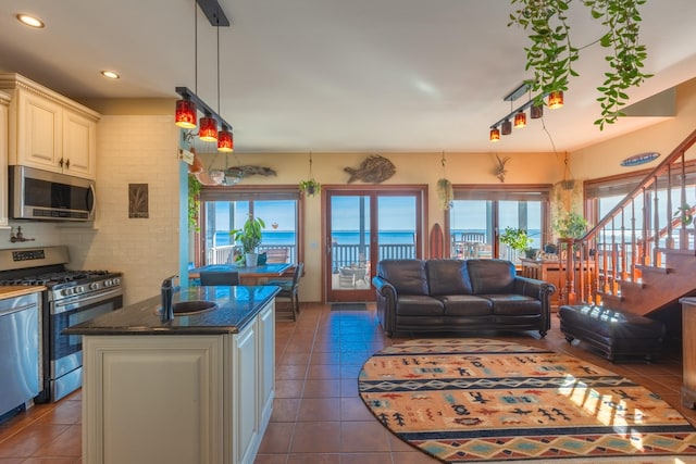 kitchen with a kitchen island with sink, dark stone countertops, stainless steel appliances, a water view, and dark tile patterned flooring