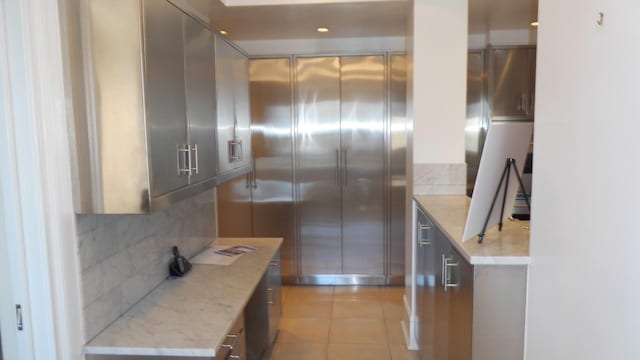 kitchen with backsplash, gray cabinetry, light stone countertops, and light tile patterned floors