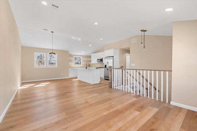 empty room with vaulted ceiling, light wood finished floors, visible vents, and baseboards