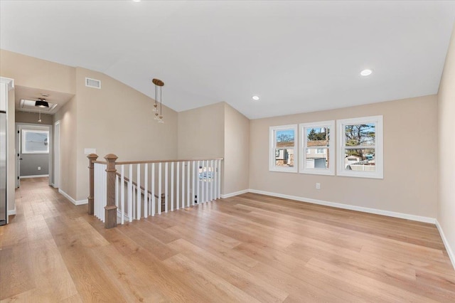 spare room with light wood-style flooring, visible vents, vaulted ceiling, and baseboards