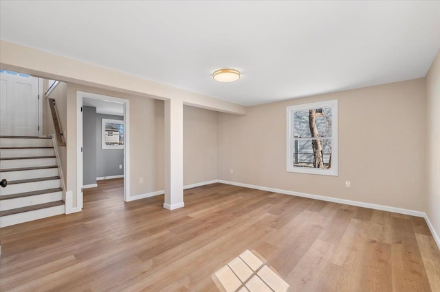 below grade area featuring stairs, a healthy amount of sunlight, light wood-type flooring, and baseboards