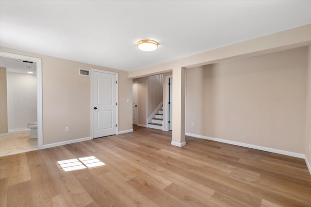 finished below grade area with light wood-style flooring, stairway, visible vents, and baseboards