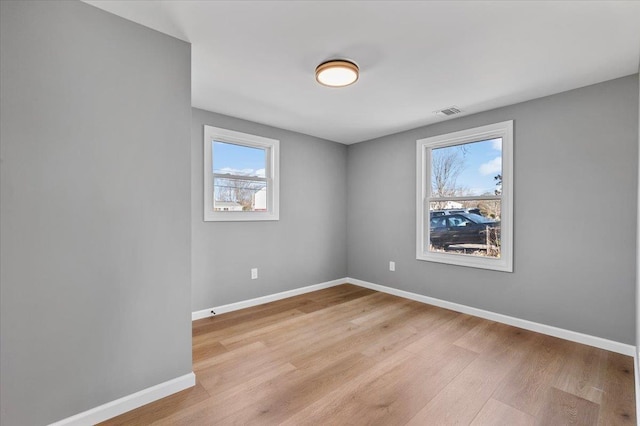 spare room featuring light wood-type flooring, visible vents, and baseboards