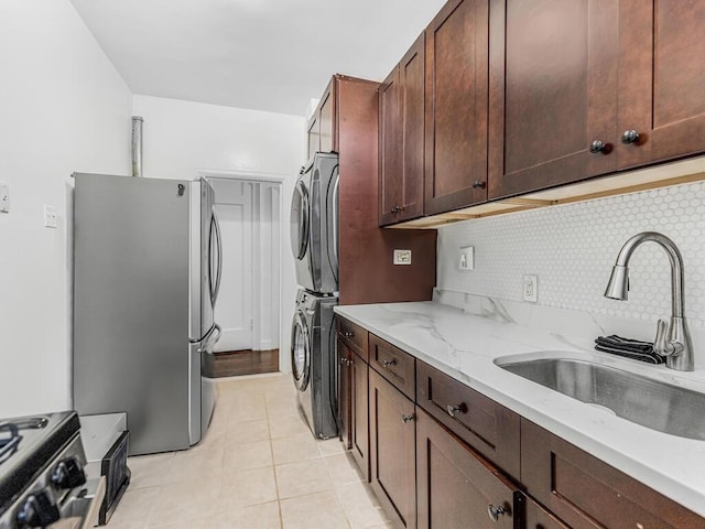 kitchen featuring stacked washer / drying machine, sink, light stone counters, stainless steel refrigerator, and stove