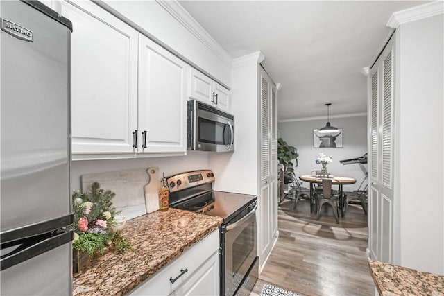 kitchen featuring appliances with stainless steel finishes, pendant lighting, white cabinetry, dark stone countertops, and ornamental molding