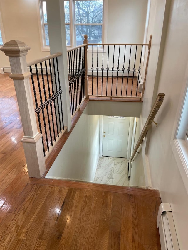 staircase with a baseboard heating unit and hardwood / wood-style floors