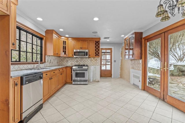 kitchen featuring appliances with stainless steel finishes, radiator heating unit, decorative backsplash, light stone counters, and french doors