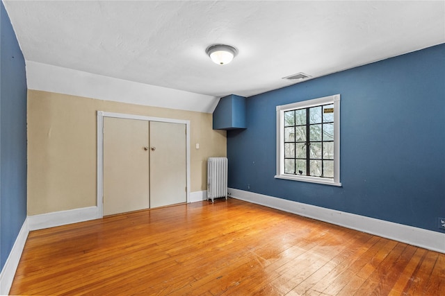 unfurnished bedroom featuring lofted ceiling, radiator heating unit, light hardwood / wood-style floors, and a closet