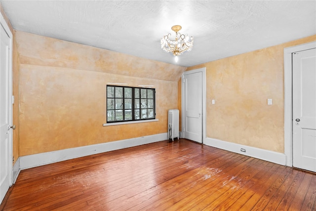 spare room featuring hardwood / wood-style flooring, vaulted ceiling, radiator heating unit, and a notable chandelier