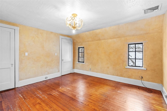 unfurnished room featuring hardwood / wood-style flooring, lofted ceiling, and a chandelier