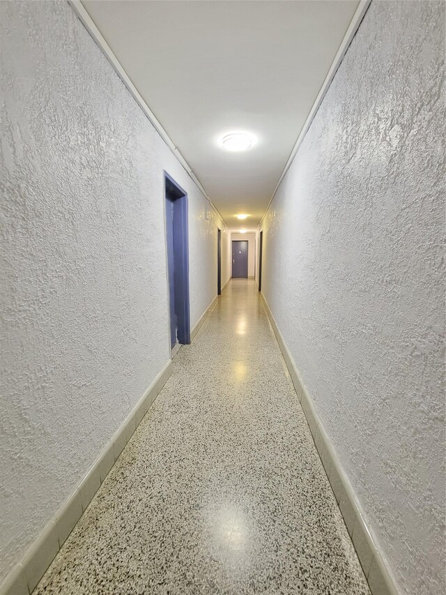 corridor with a textured wall, speckled floor, and baseboards