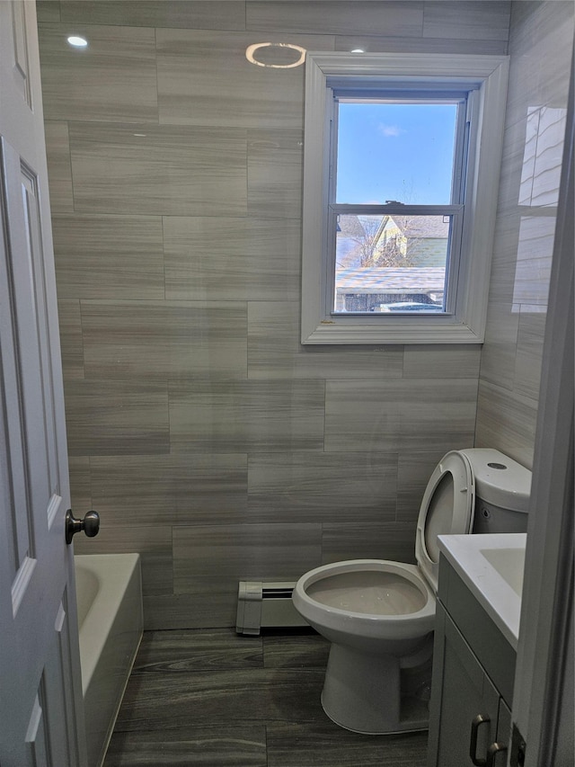 bathroom with toilet, tile walls, vanity, a bathtub, and a baseboard heating unit