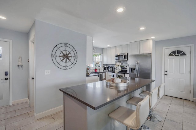 kitchen with appliances with stainless steel finishes, a kitchen island, tasteful backsplash, white cabinetry, and a kitchen breakfast bar